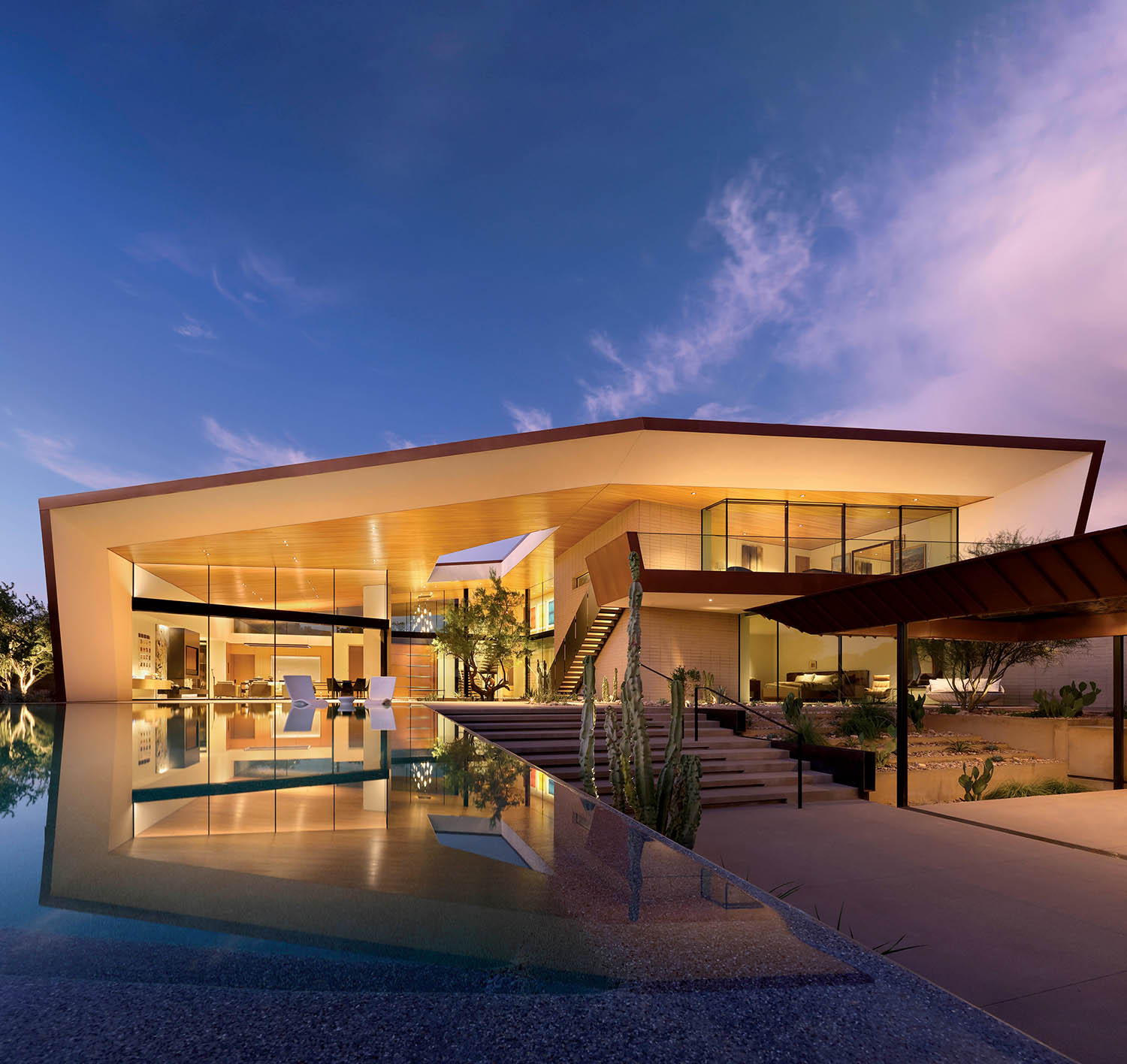 Modern luxury home at dusk with sleek, angular architecture. Large glass windows reflect a tranquil pool; a serene ambiance under a twilight sky.