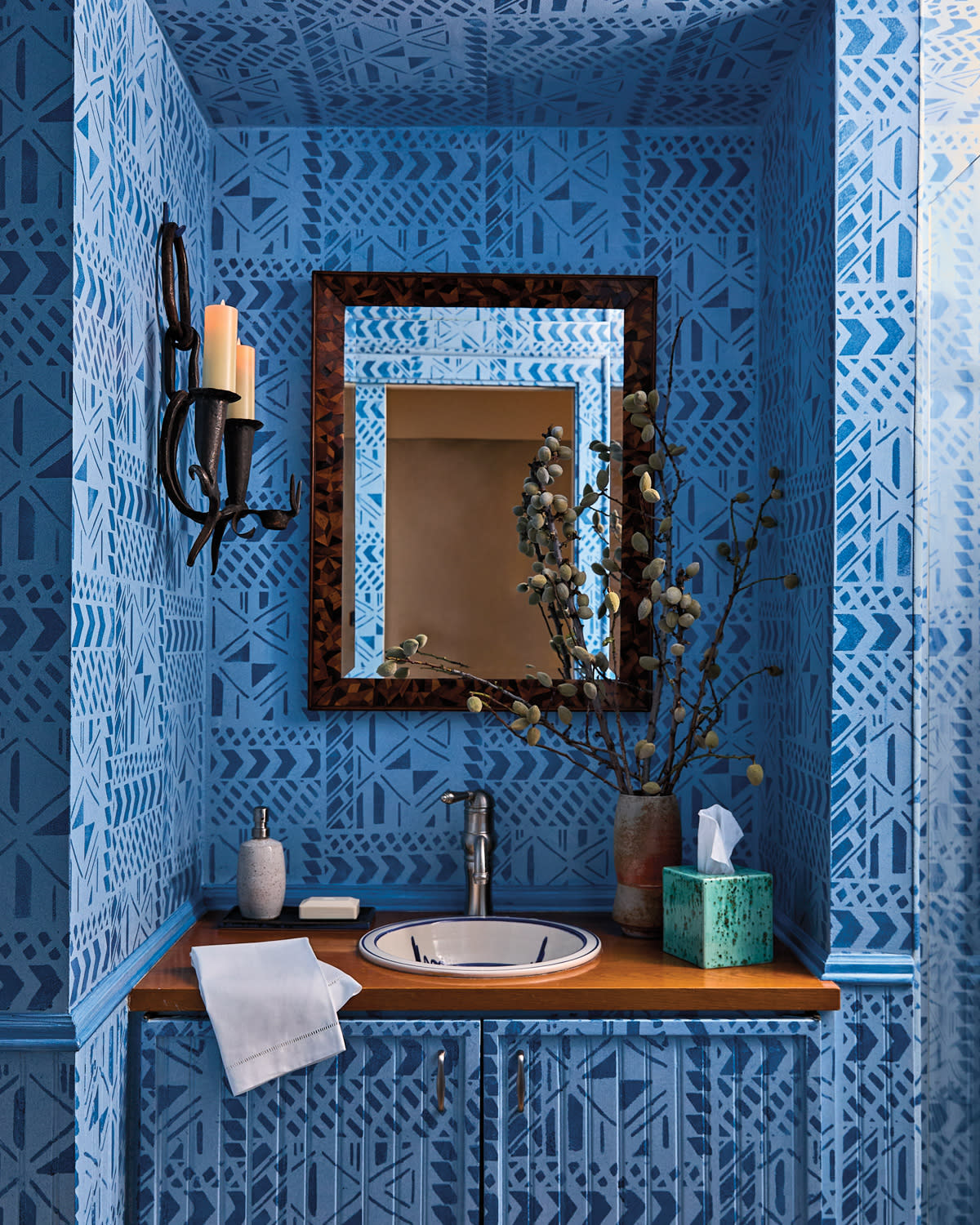 A small, stylish bathroom features blue geometric wallpaper, a wooden countertop, and a sink. 