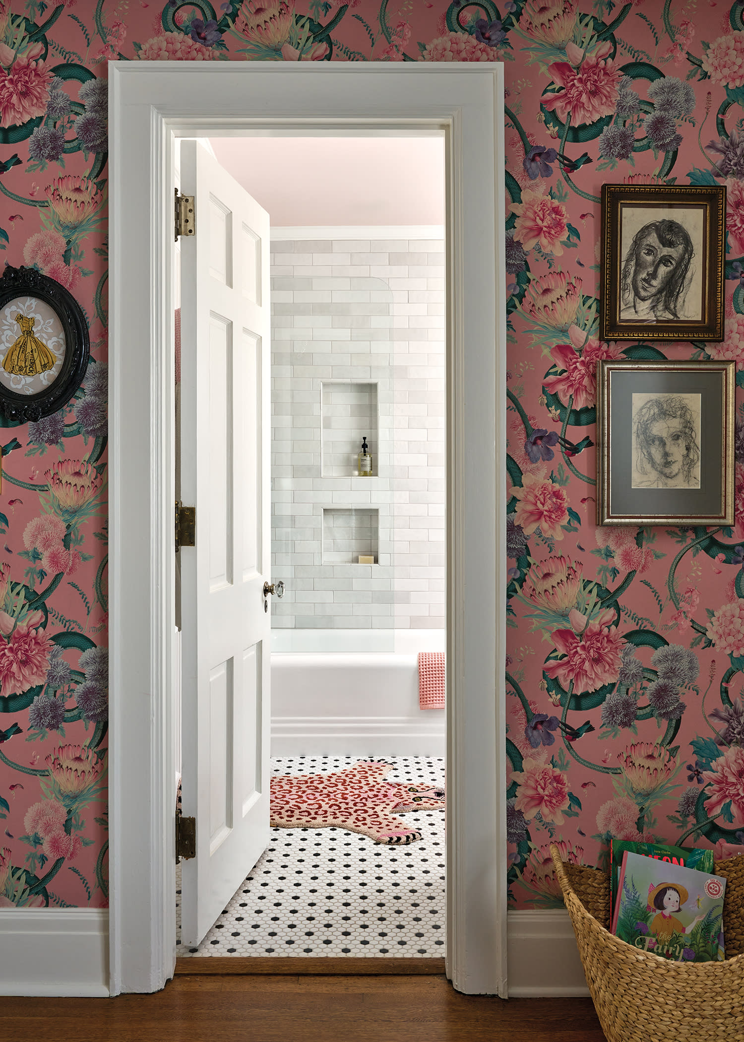 pink floral wallpaper with a trio of vintage prints flank the doorway into a white bathroom